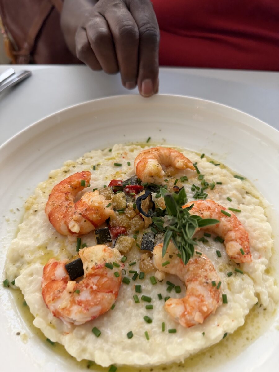 A plate of prawn risotto being finished with herbs at a restaurant table