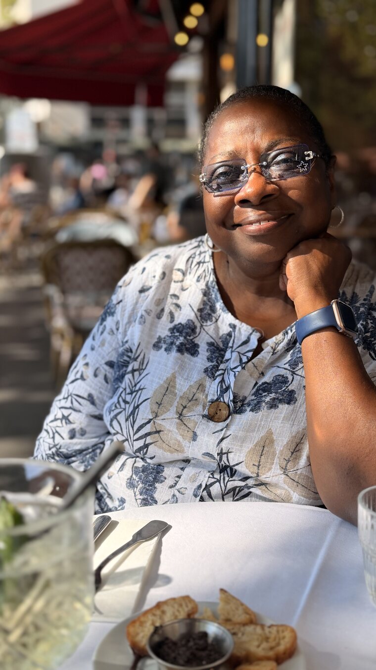 Sandra smiling at a cafe table in the late afternoon sun